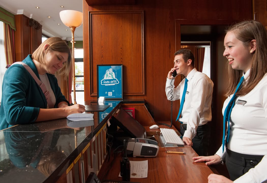Living Hotels AZUBI-HOTEL: Empfang mit Kevin, Melanie und Gast. Foto: Andy Rumball